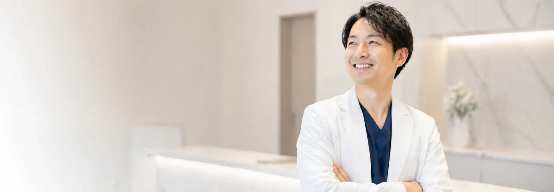 白衣を着た医師が、明るい医療施設で笑顔で立っている